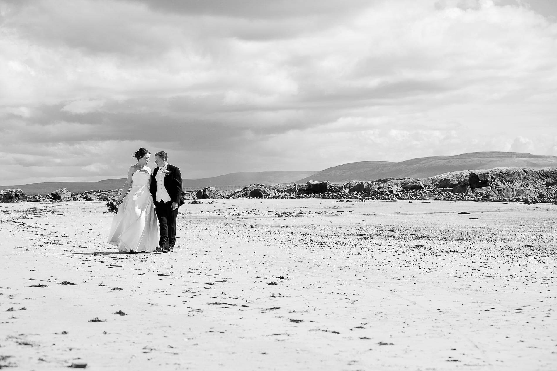 Bride and groom walking and talking to each other on a beach